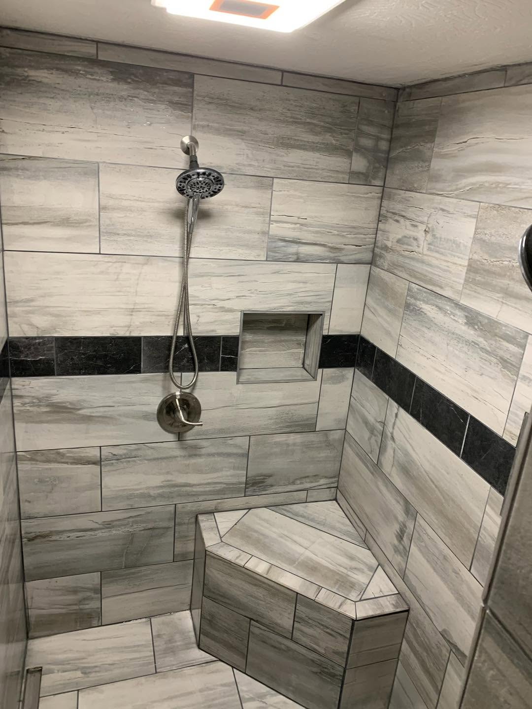 Walk-in shower with gray tile, inset shelf, and built-in corner seat